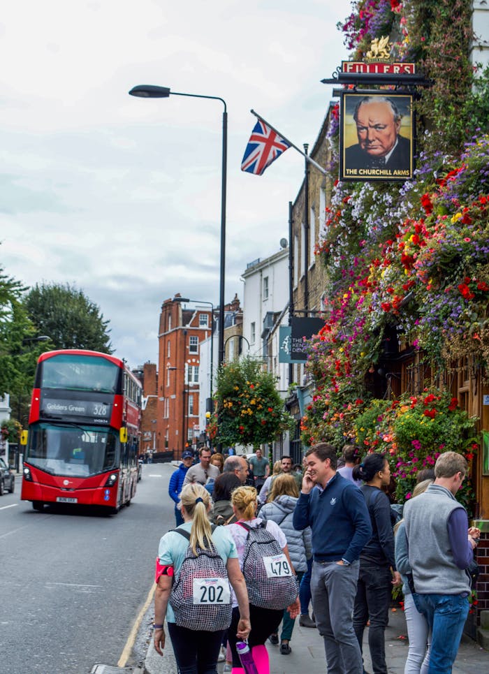 A bustling London street with a red double-decker bus past The Churchill Arms pub with hanging flowers.